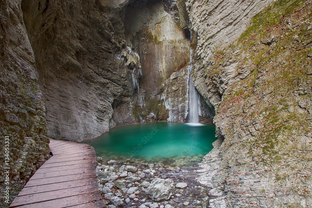 Fototapeta premium Wood bridge to frozen Waterfall and green colour river Pool