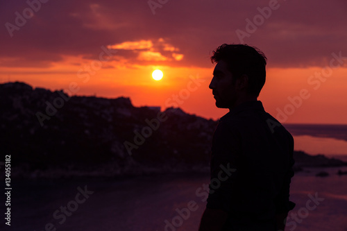 man standing thinking back light sunset lighting side view summer evening beach