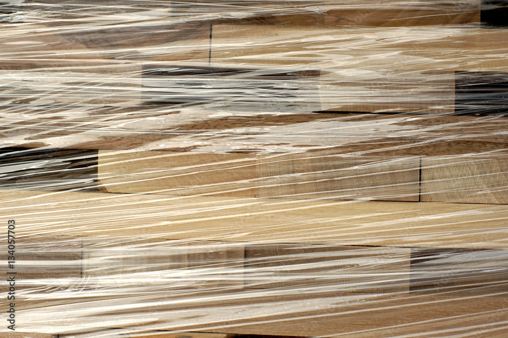 Fototapeta premium Wooden planks stacked in rows wrapped in plastic foil