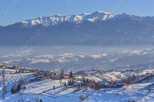 Magnificent rural view with the snowy Rucar-Bran pass in the valley of Bucegi mountains on a cold winter day, Pestera village, Brasov county, Transylvania region, Romania.