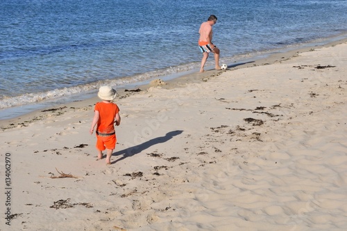 Un petit garçon joue au football avec un homme sur une plage de Bretagne