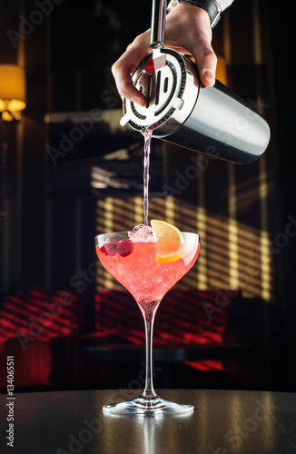 Barman at work, preparing cocktails. pouring cosmopolitan to cocktail glass.