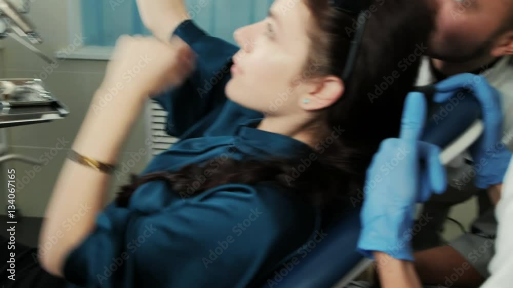 Woman sitting in a dental chair makes a photo with the medical staff. A doctor and a nurse in uniform sitting behind the patient and posing for the camera. They smile and look in white smartphone. The