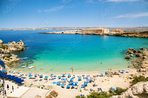 Blue umbrella on tropical beach with white sand, turquoise sea water and blue sky at deserted island in Malta, Paradise bay.