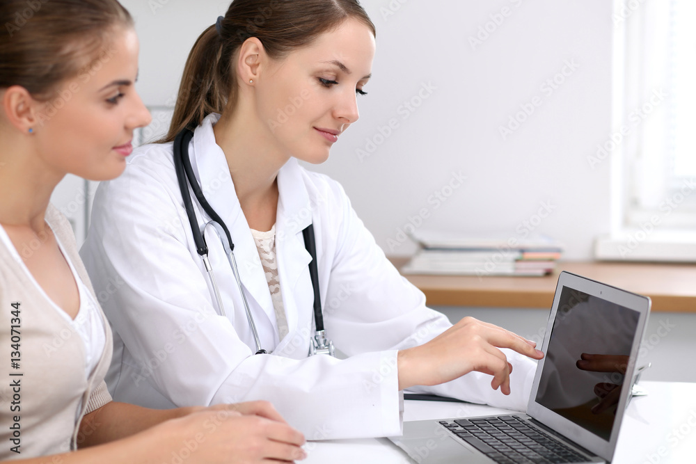Doctor and patient sitting at the desk. Physician pointing into laptop computer. Medicine and health care concept Doctor and patient sitting at the desk. Physician pointing into laptop computer. Medicine and health care concept