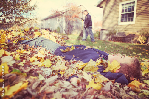 Young boy daydreaming in a pile of fall leaves while his father
