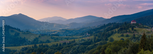 Wide sunset panorama of the Carpathian mountains. Ukraine. Small hotel on hill at the right part of image as detail.