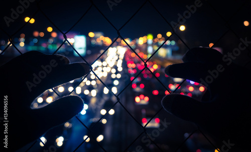 eagerness to freedom, hands to pinch chain-link fence, urban background with bokeh photo