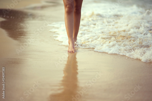 Leg girl walking on the beach with impact wave