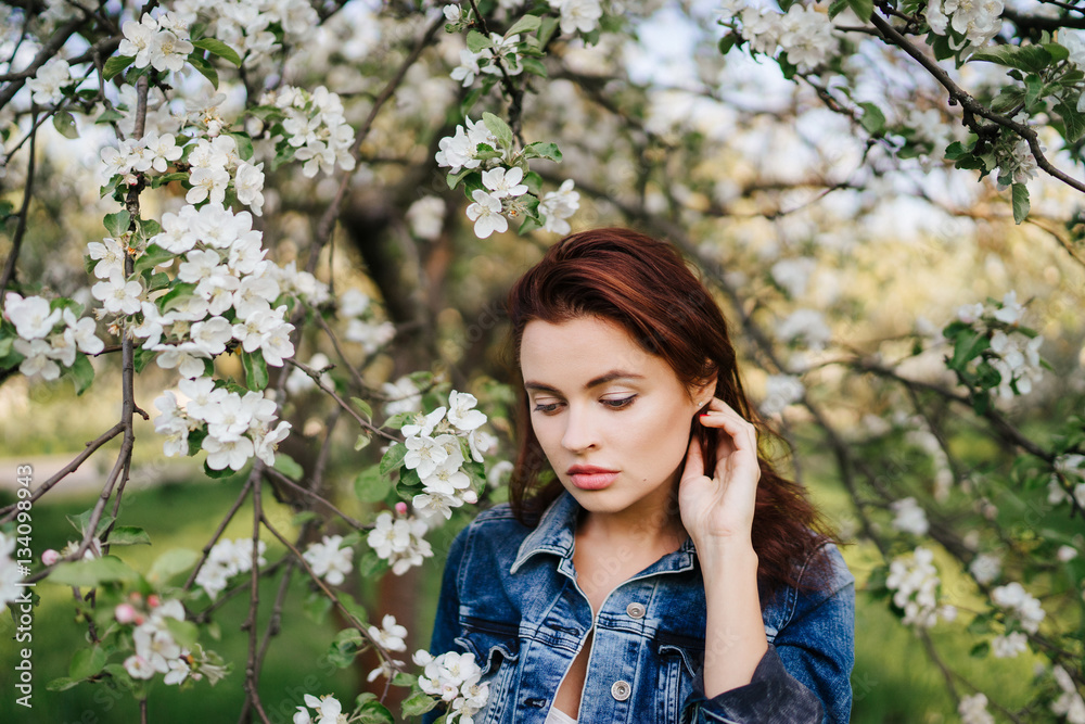 Young pretty serious caucasian woman in jeans jacket standing near blooming spring tree. Youth, freshness, beauty, happiness concept. Healhty hair, clean skin. Young pretty serious caucasian woman in jeans jacket standing near blooming spring tree. Youth, freshness, beauty, happiness concept. Healhty hair, clean skin.