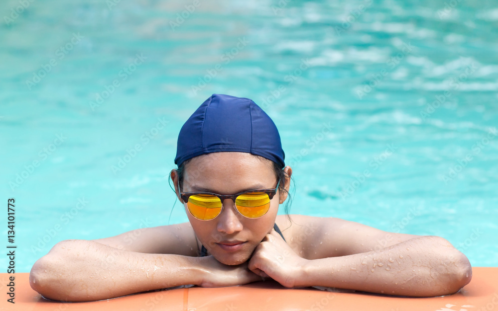 Girl in bikini and swimming cap leaning on the edge of the pool