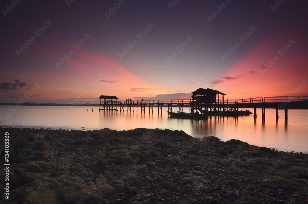 Beautiful sunset over wooden jetty with silhoutte of man fishing