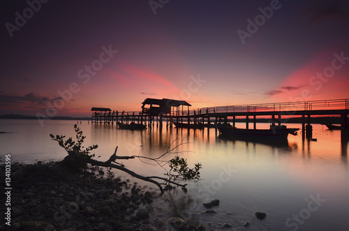 Beautiful sunset over wooden jetty with silhoutte of man fishing © nelzajamal