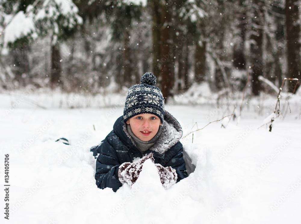 Kid playing winter game. Boy lying on snow in the forest
