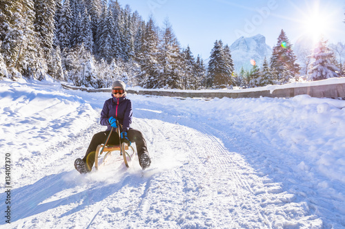 Cheerful girl riding a sled downhill, snow, sunny winter landscape
