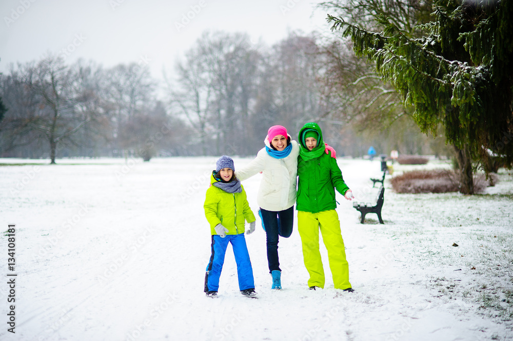 Young woman and two of her sons cheerfully spend time in the park in winter day.