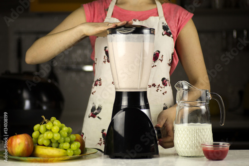 A beautiful woman preparing a milk coctail with fruits in the kitchen.