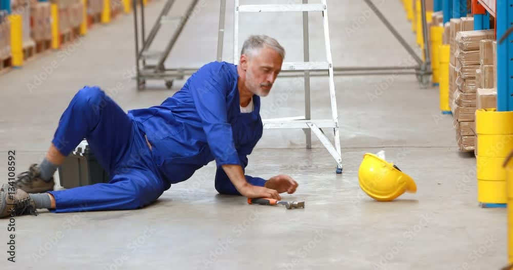 Male warehouse worker falling off ladder while working