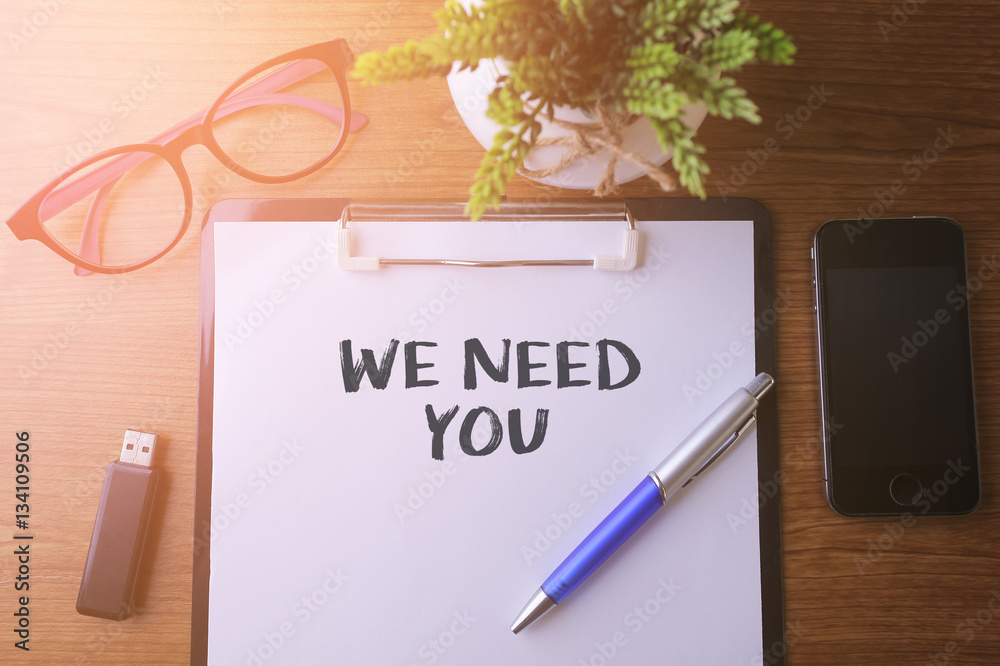 Fototapeta premium Office desk with a paper written WE NEED YOU with pen, glass, sm