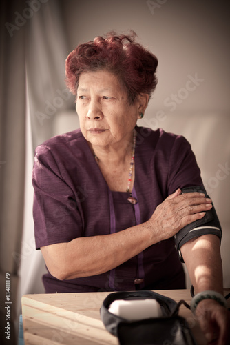 Asian senior woman checking blood pressure with window light and photo