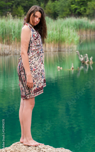 Fototapeta Naklejka Na Ścianę i Meble -  Portrait of a young girl on a rock in a lake wearing a sarong