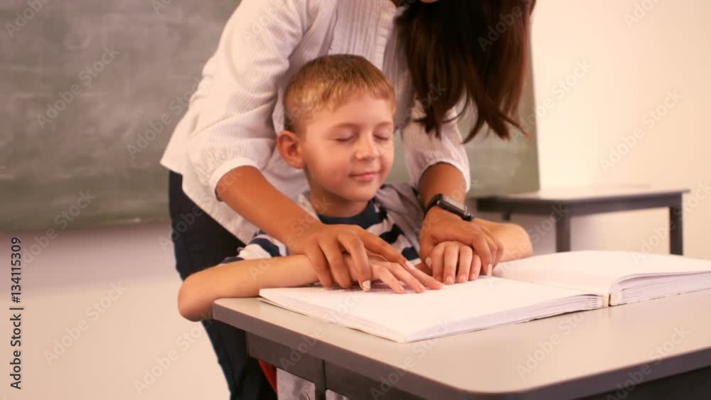Teacher helping a blind schoolboy with his homework in classroom Teacher helping a blind schoolboy with his homework in classroom