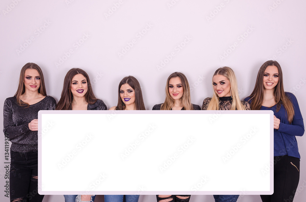 Group of young girls holding a big white board and looking at th Group of young girls holding a big white board and looking at th