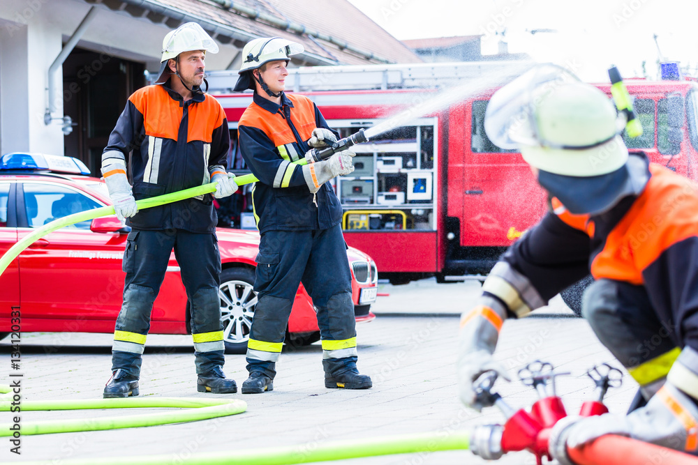Fototapeta premium Feuerwehrmänner löschen einen Brand mit Wasserschlauch