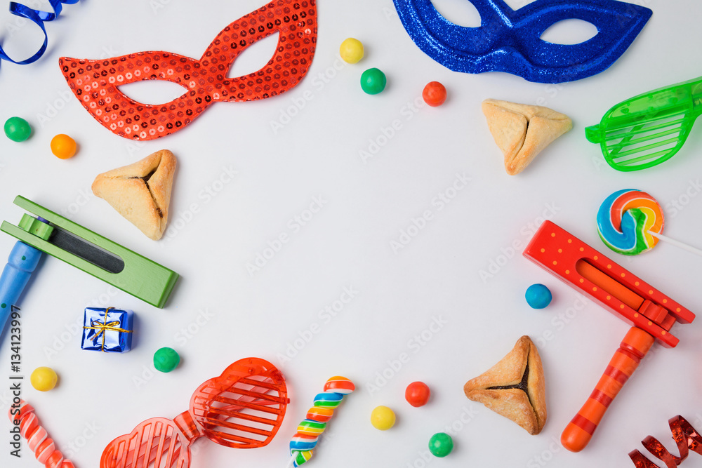 Jewish holiday Purim concept with hamantaschen cookies, carnival mask and noisemaker on white background. View from above