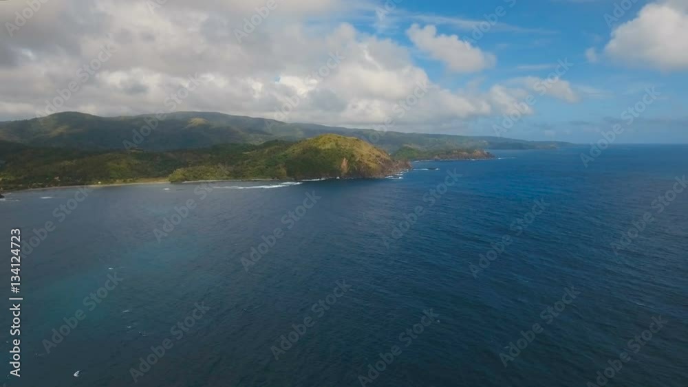 The coast of the tropical island with the mountains and the rainforest on a background of ocean with big waves.Aerial view: sea and the tropical island with rocks, beach and waves. Seascape: sky The coast of the tropical island with the mountains and the rainforest on a background of ocean with big waves.Aerial view: sea and the tropical island with rocks, beach and waves. Seascape: sky
