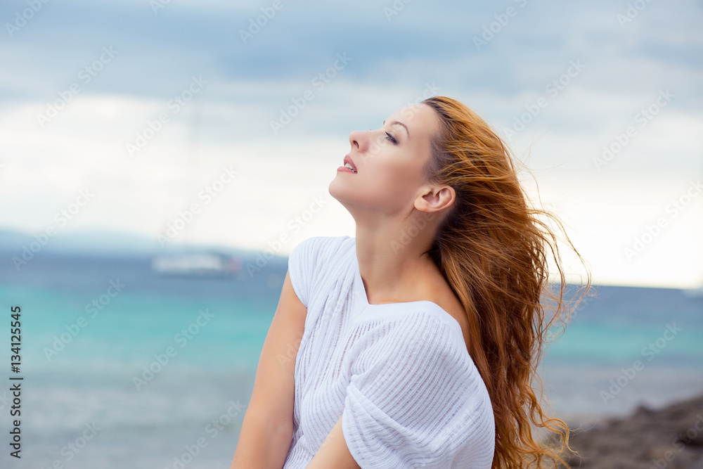 Woman relaxing at beach enjoying summer freedom with hair in the wind by the water seaside Woman relaxing at beach enjoying summer freedom with hair in the wind by the water seaside