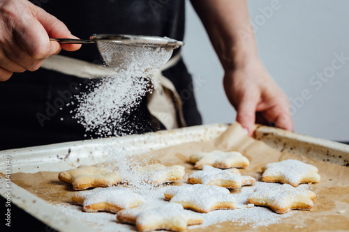 Slika na platnu Hands of cook adding powdered sugar to cookies as a topping