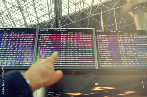 Flights information board in airport terminal. Man points a finger at flight information board at the airport. Background flight schedules.