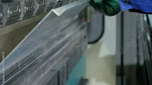 Man working with sheet metal on CNC hydraulic press brake. He puts the part and bends it into a large machine at an angle