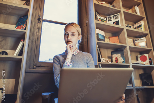 beautiful woman is using her laptop computer in front of a bookcase 