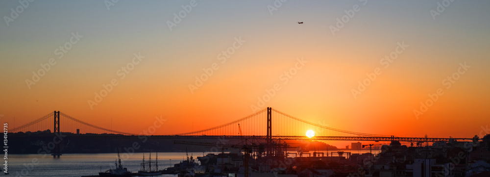 Obraz premium Sonnenuntergang hinter der Ponte 25 de Abril, die Brücke über den Tejo in Lissabon ( mit Industriehafen im Vordergrund)