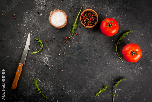 Dark gray stone (concrete) kitchen table with a knife, spices, herbs and vegetables. cooking background. Top view, copy space