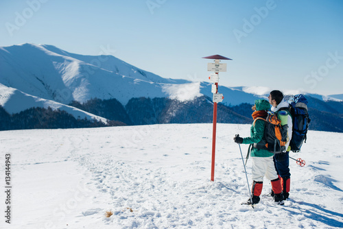 Couple with backpacks is hiking in snowy winter mountains
