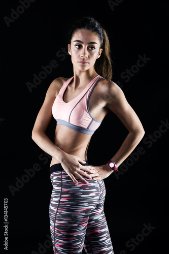 Fit and sporty young woman stretching on black background.