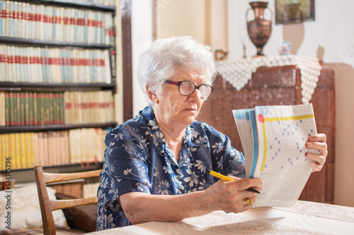 Senior woman sitting at a table wearing reading glasses concentr