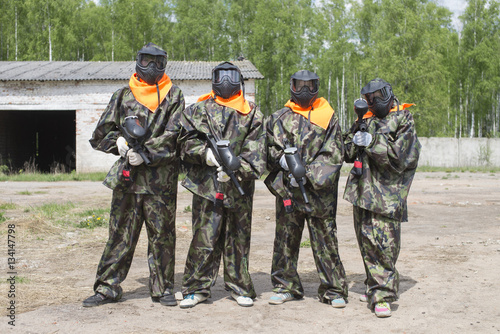 Paintball Team of four men in camouflage suits with paintball markers in hand lined up for growth