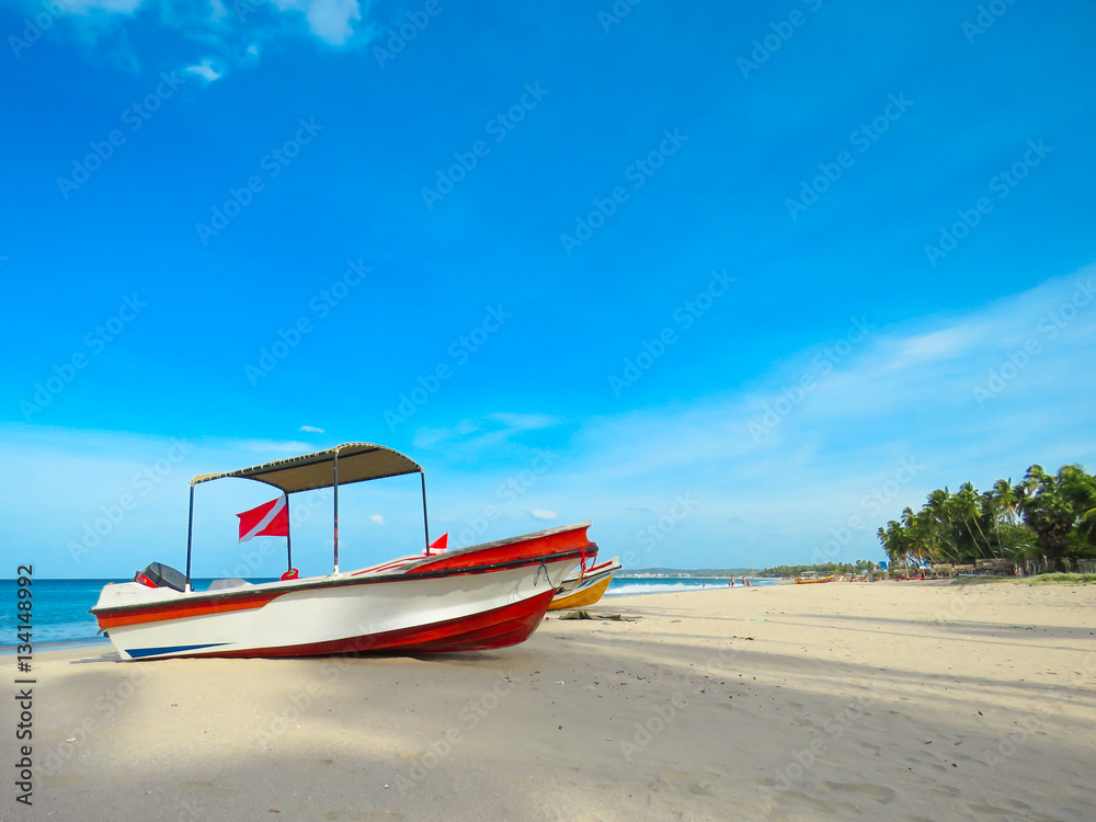 Rescue Fishing Boat on the beautiful white sand sandy beach with coconut trees and blue sky with clouds in background Rescue Fishing Boat on the beautiful white sand sandy beach with coconut trees and blue sky with clouds in background