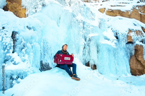 Happy young man playing the harmonium on a frozen waterfall photo
