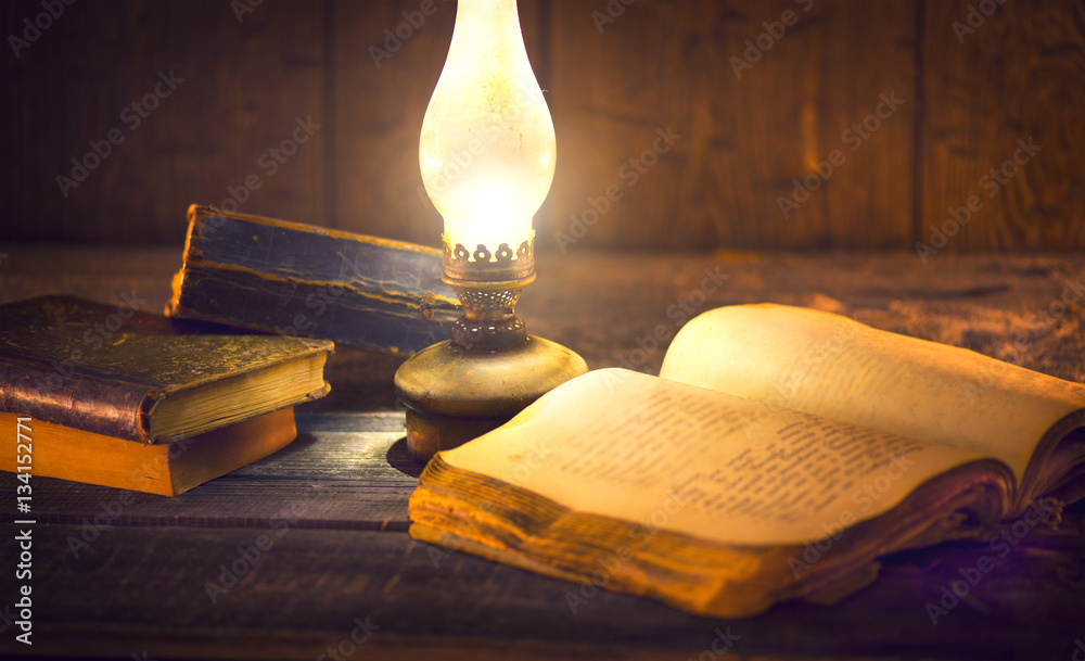 Foto Stock Old oil lamp and old books in darkness. Vintage kerosene lantern  and open old book with blank pages on wooden table | Adobe Stock