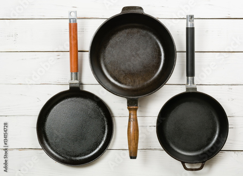 Several empty cast-iron frying pans on a white wooden background. View from above.