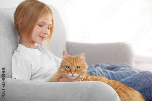 Cute little girl with red fluffy cat on sofa in room