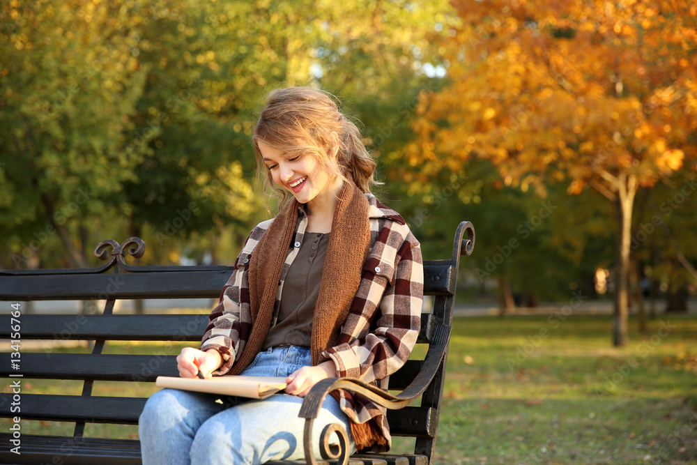 Young female artist drawing sketch while sitting on bench in beautiful park Young female artist drawing sketch while sitting on bench in beautiful park