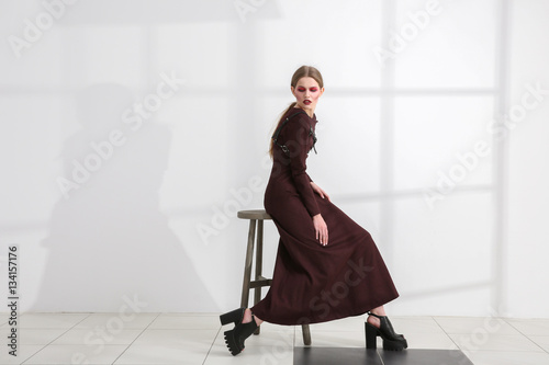 Young extravagant model sitting on chair near light wall