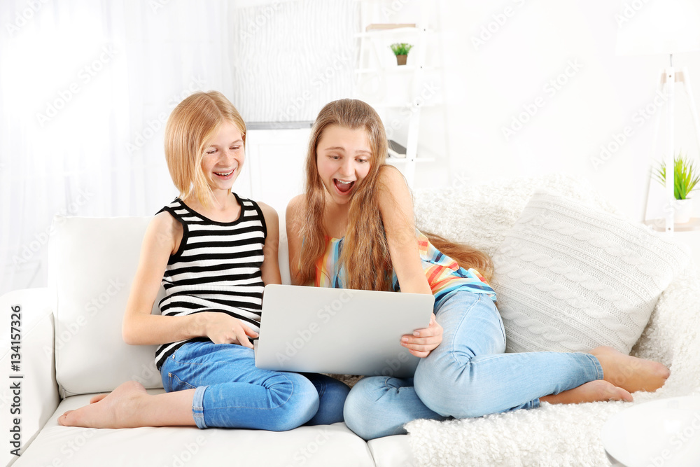 Two cute girls with laptop sitting on sofa