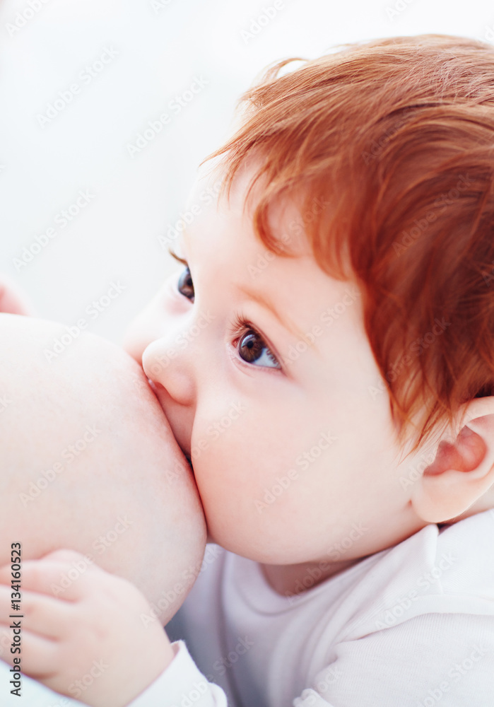adorable ginger baby with big eyes suckles breast and looks at mom adorable ginger baby with big eyes suckles breast and looks at mom